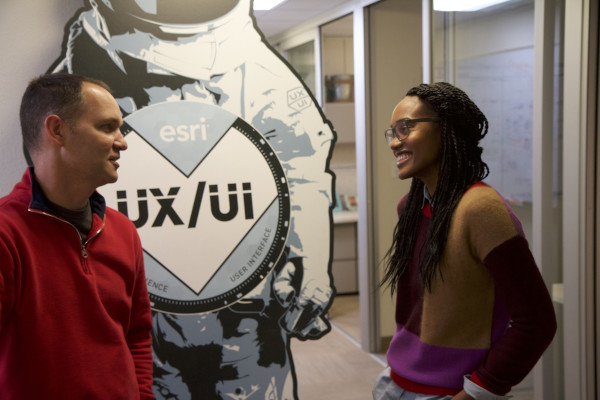 Woman and man talking in hallway in front af a esri logo spacesuit Woman and man talking in hallway in front af a esri logo spacesuit