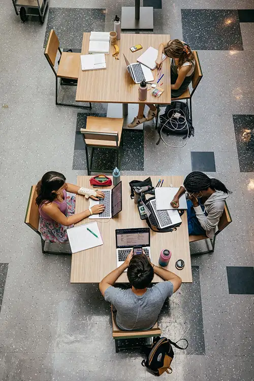 Overhead view of diverse students at tables working on laptops