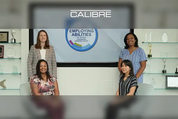 diverse women sitting and standing in front of sign Emloying Abilities at work