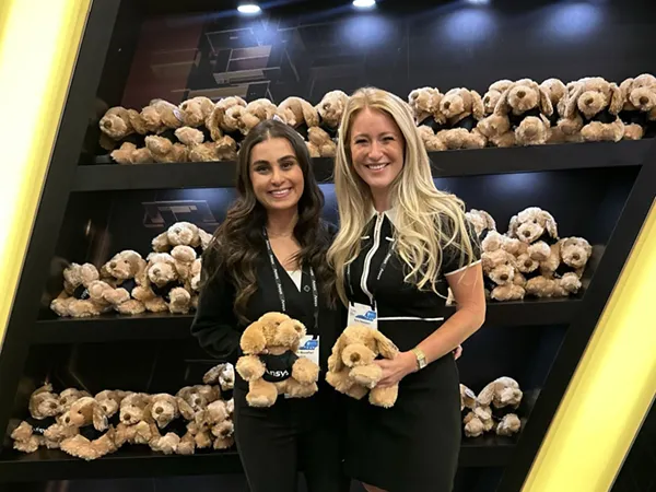 Women holding stuffed dogs in front of a display of stuffed dogs at a display booth
