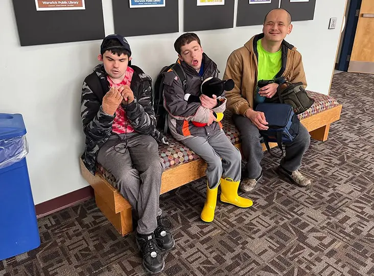 man and two teens sitting on soft bench in hall way smiling