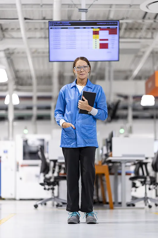 Woman with hair pulled back and wearing protective glasses stands in front of a work environment