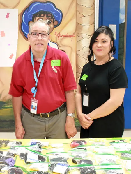Man and woman standing in front of a table with treat bags wearing business casual attire and work badges