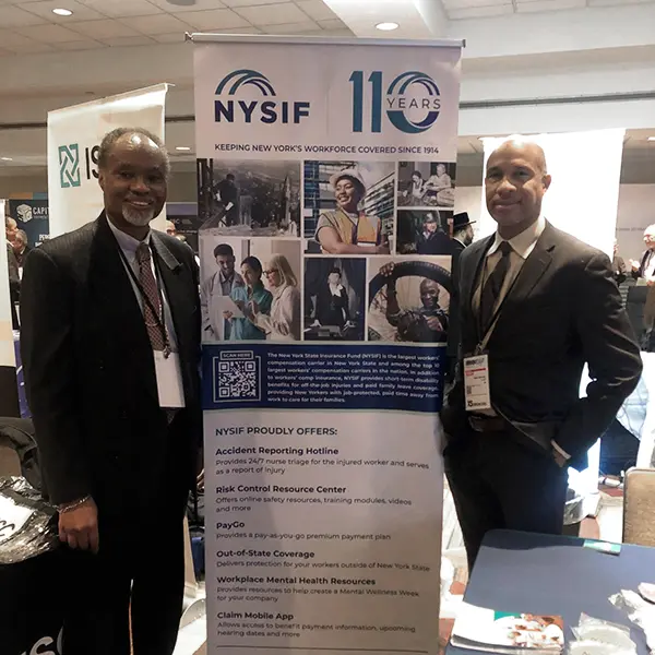 two african american men in business suits stand in front of a NYSIF banner that lists services