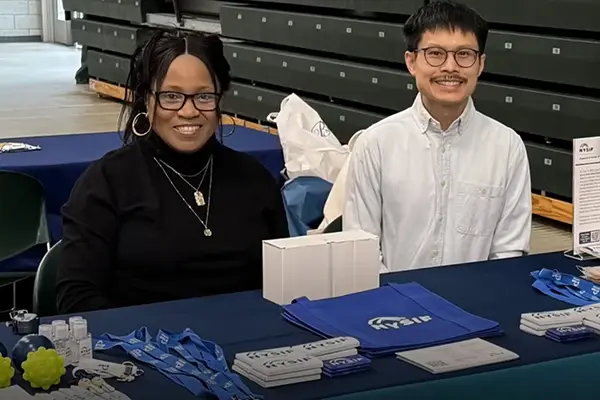 african american woman and asian man sit behind table at a job fair with nysif swag