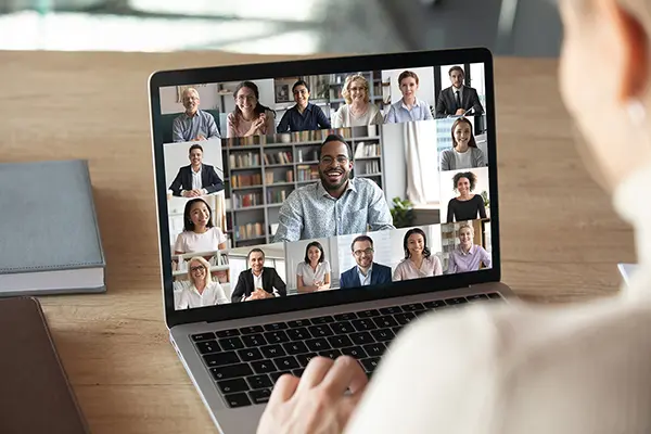 woman looking at a computer screen with multiple diverse team members on a video meeting