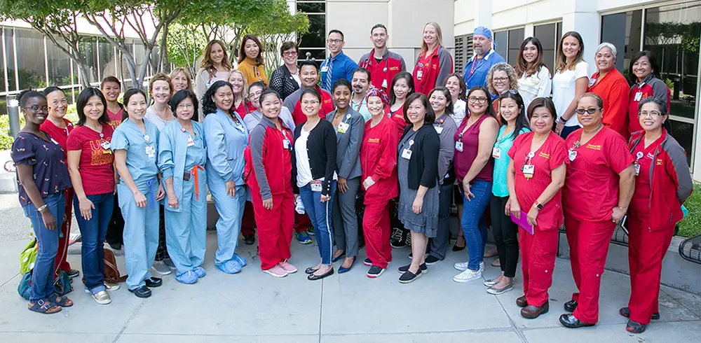 Large group of diverse smiling group of men and women in red and blue surgical scrub outdoors in a courtyard